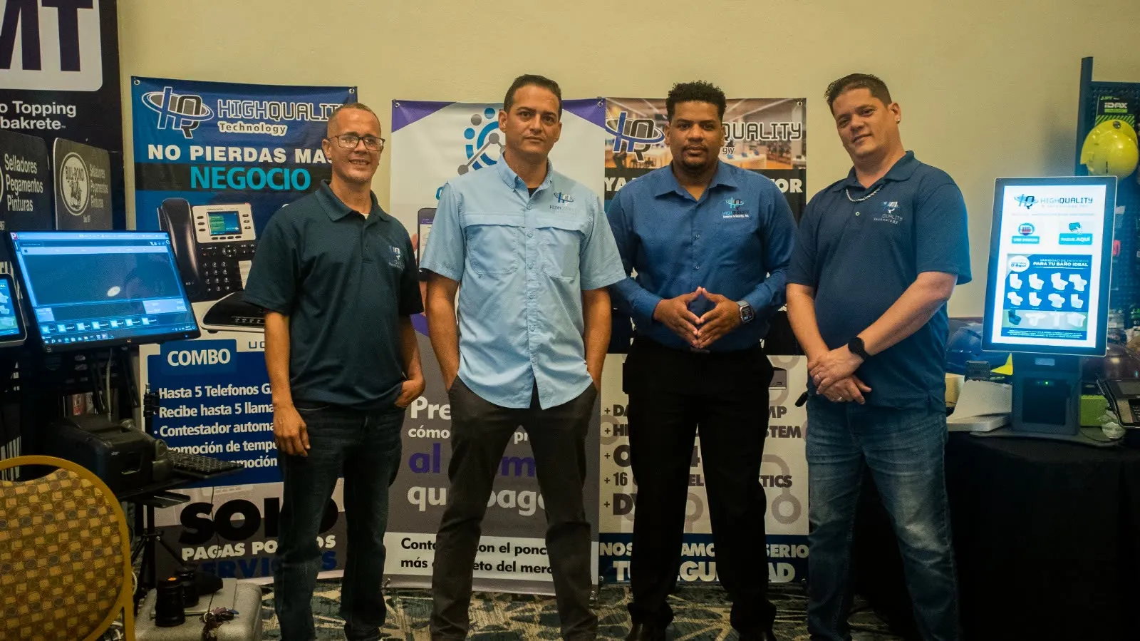 Cuatro integrantes del equipo de High Quality en su stand, junto a un cuadro telefónico, una caja registradora y un kiosko de autoservicio